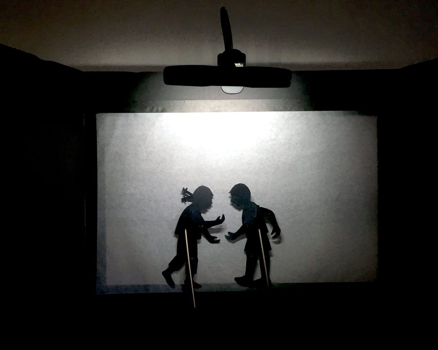 Inside of a shadow puppet screen showing a girl and boy puppet with holding rods