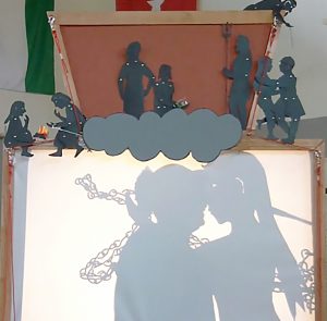 Shadow puppet screen showing a man kissing a life size puppet, project from an overhead project.