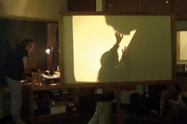 Screen showing child pushing up a boulder projected from overhead projector