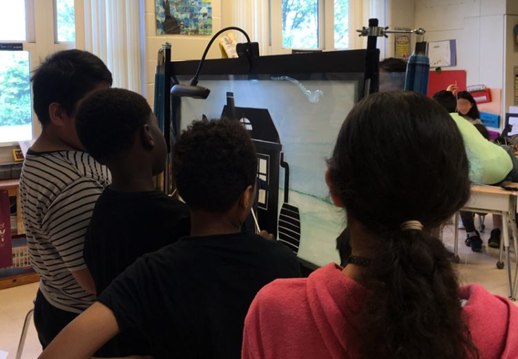 Children seen on the back acting out a shadow puppetry scene with transparent scrolling background