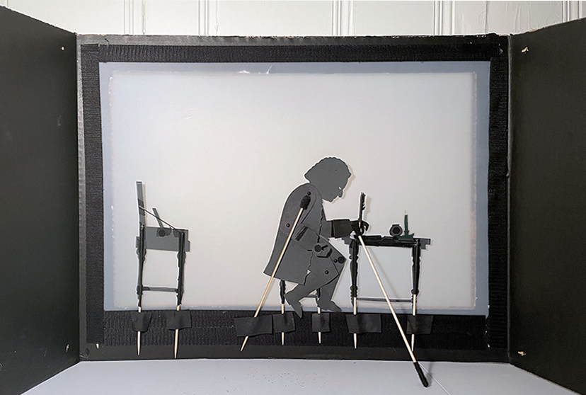 Inside of a desk top theater showing Bach at writing desk with quill, ink pot and candle and clavichord behind him