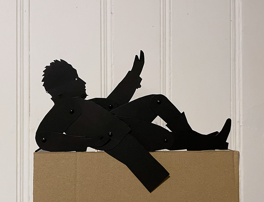Silhouette puppet of a man laying on his back, supporting himself on one arm and looking up