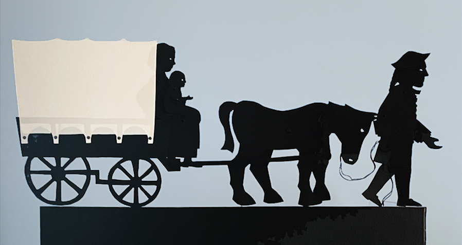 Silhouette puppets showing a man holding the reigns of a horse, which pulls a covered wagon with a woman on the front seat holding a little child.