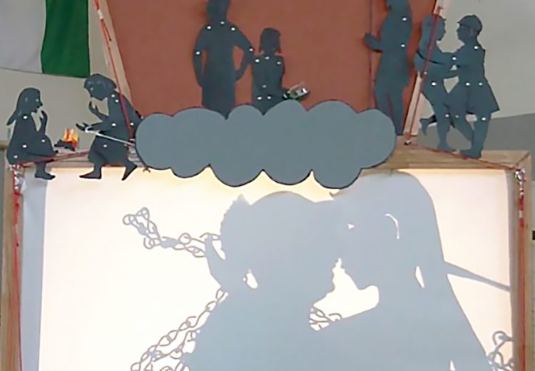 Shadow puppet screen showing a man kissing a life size puppet, project from an overhead project.