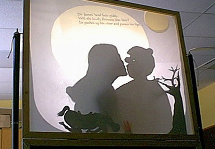 Teacher kissing a puppet of a knight, projected from an overhead projector