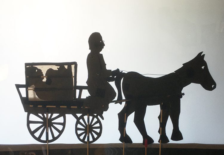 shadow puppets of man riding a horse and wagon
