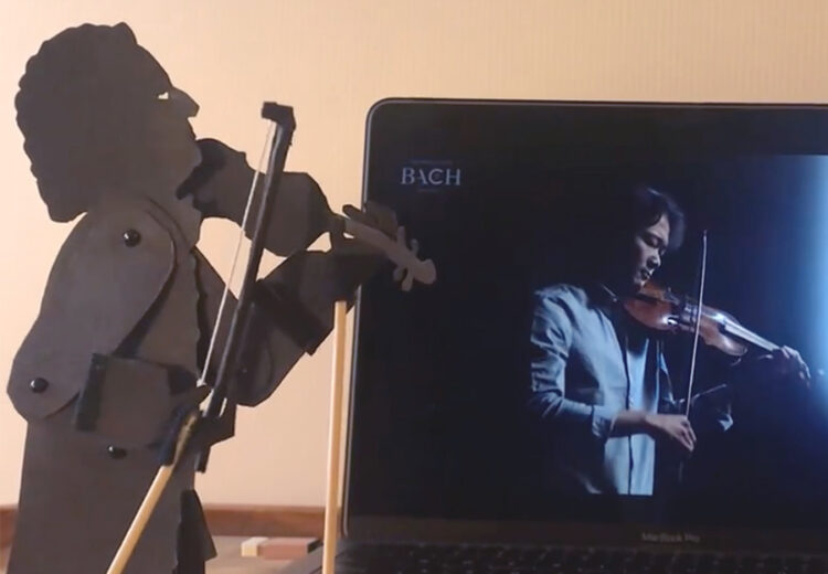 Puppet of Bach playing violin with violinist on laptop