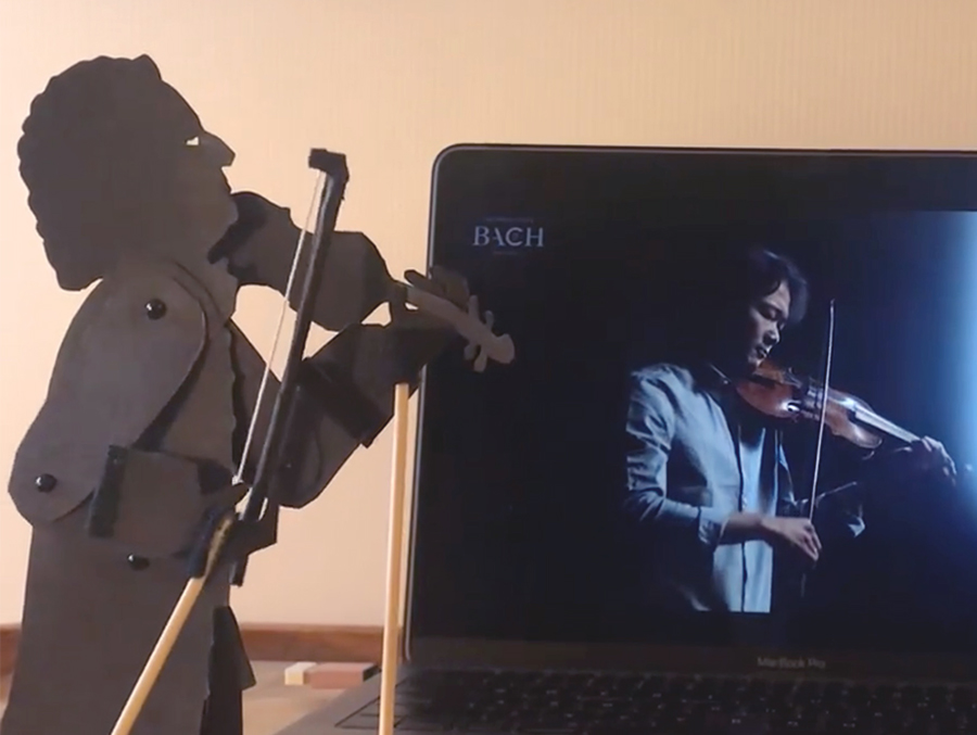 Puppet of Bach playing violin with violinist on laptop