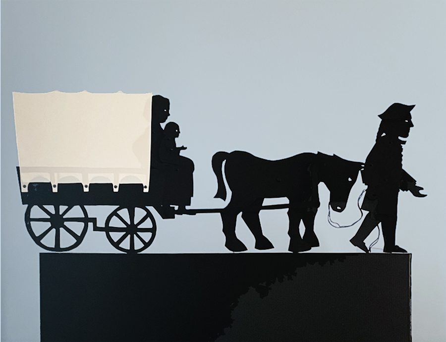 Silhouette puppets showing a man holding the reigns of a horse, which pulls a covered wagon with a woman on the front seat holding a little child.
